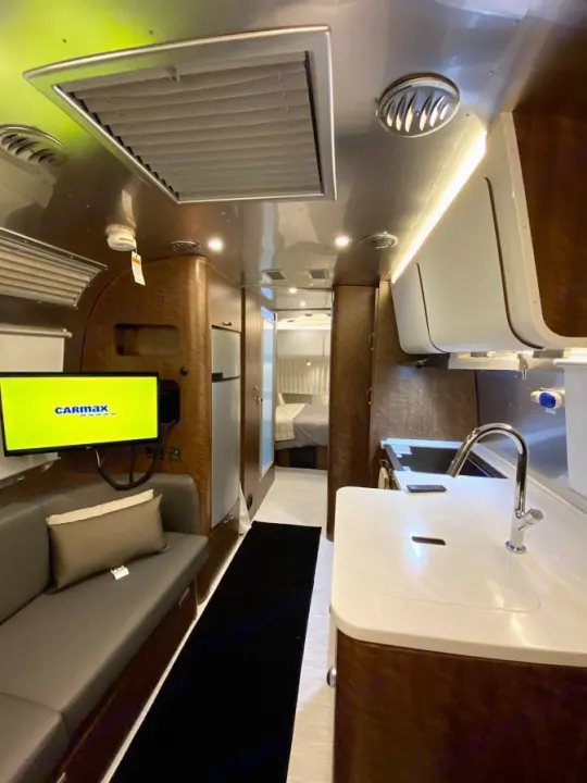 Modern RV rental interior: Kitchen, living area with TV, and hallway leading to a cozy bedroom setup.. Airstream Globetrotter 2020