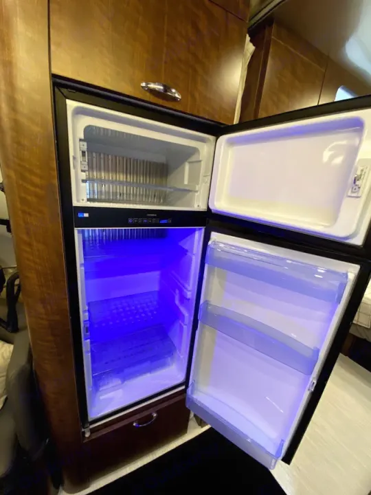 Inside this RV rental, an open refrigerator with blue lighting reveals the freezer and compact storage for your travels.. Airstream Globetrotter 2020