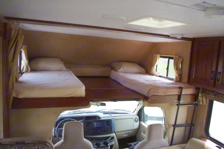 Inside this **RV rental**, two cozy bunk beds are positioned above the driver's cab, providing a practical sleeping area for any **camper** trip.. Forest River Sunseeker 2015
