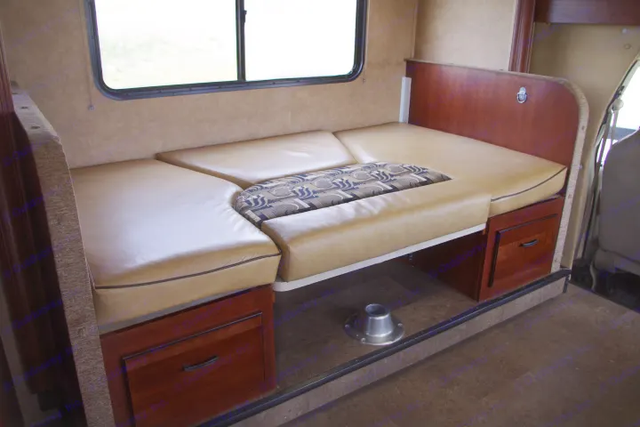 RV rental interior: Convertible U-shaped dinette with tan cushions, patterned insert, wood storage, and a large window.. Forest River Sunseeker 2015