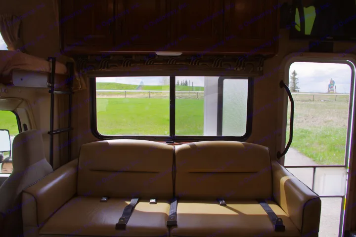 Spacious rv rental interior with comfy bench seat and large windows showcasing a scenic green landscape and distant structure.. Forest River Sunseeker 2015