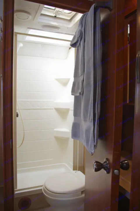 Inside an RV rental: a compact bathroom with a toilet, shower, and neatly folded towels on a wooden counter.. Forest River Sunseeker 2015