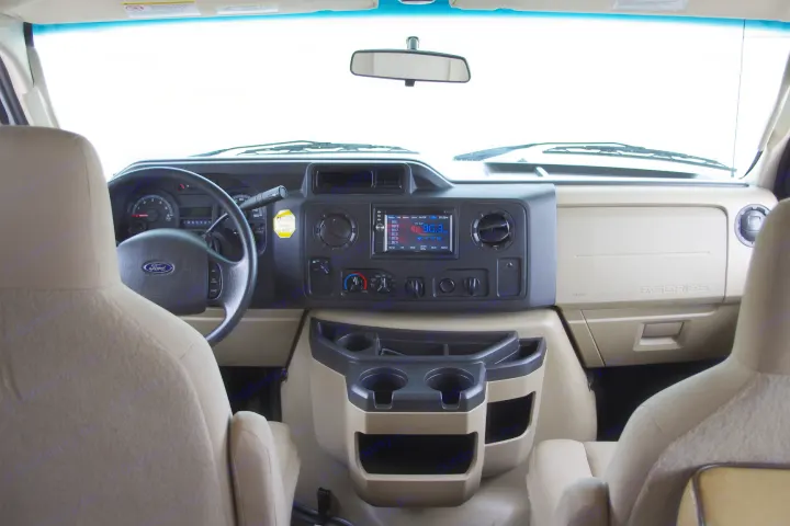 Inside a Ford E-Series RV rental: driver's cockpit with steering wheel, dashboard, radio, and cup holders.. Forest River Sunseeker 2015
