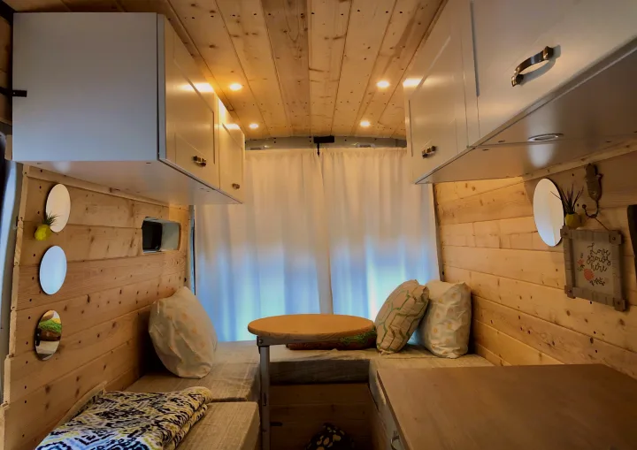 Cozy wooden RV rental interior: overhead cabinets, bench seating, warm lighting, and a versatile table for your travels.. Ford Transit 2015