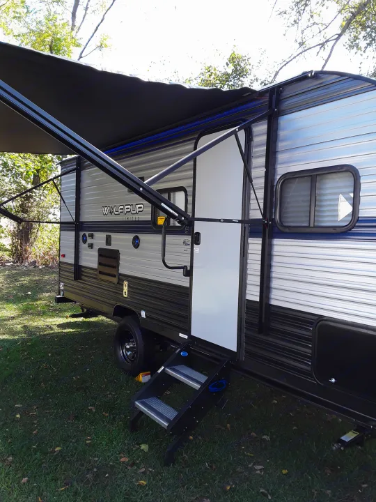 This **RV rental**, a Wolfpup travel trailer, features an extended awning with blue lights and entry steps, parked on grass.. Forest River Wolf Pup 2020