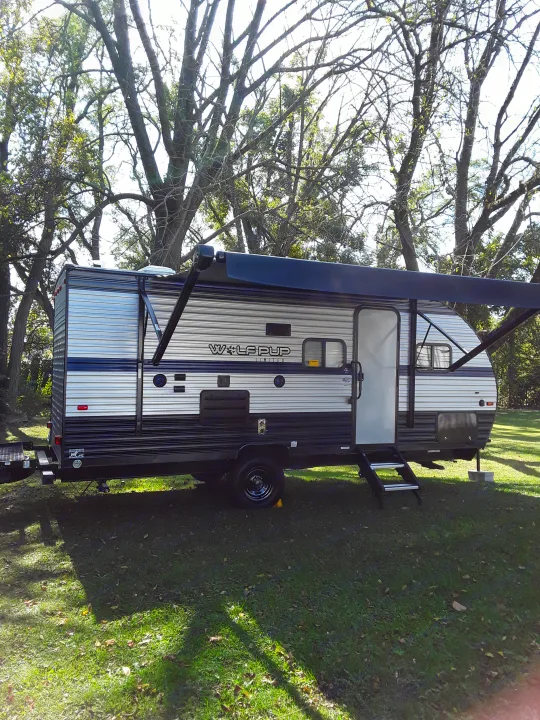 Grey and black Wolf Pup travel trailer, an RV rental, parked on grass with trees. Awning extended, ready for camping.. Forest River Wolf Pup 2020