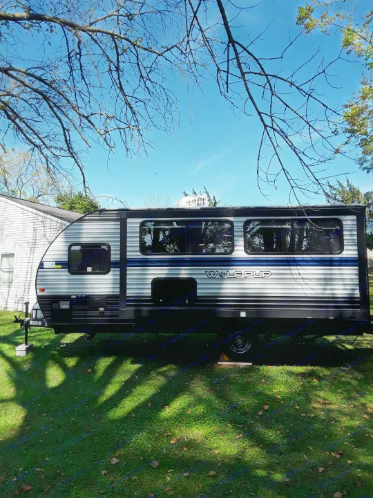 A sleek Wolf Pup travel trailer, perfect for an RV rental, parked on green grass under a clear blue sky and bare trees.. Forest River Wolf Pup 2020