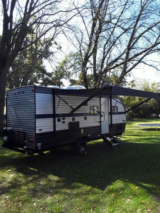 This RV rental, a travel trailer, is parked at a sunny campsite with its awning extended and trees overhead.. Forest River Wolf Pup 2020