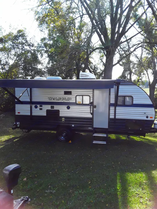 This Wolf Pup travel trailer, an RV rental, is set up on grassy ground under a large shade tree, ideal for camping.. Forest River Wolf Pup 2020