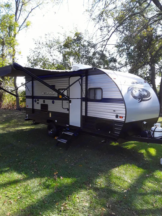 This modern Wolf Pup travel trailer, ideal for your next RV rental, is parked on grass with its awning open.. Forest River Wolf Pup 2020