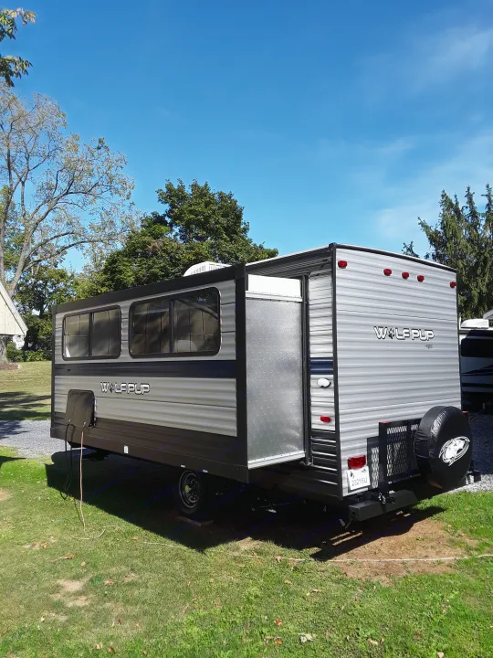 Wolf Pup travel trailer RV rental parked on grass with awning extended. Sunny day, clear sky. Ready for outdoor adventures.. Forest River Wolf Pup 2020