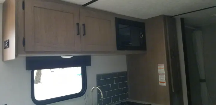Experience comfort in this RV rental kitchen: modern cabinets, built-in microwave, sink, and large window.. Keystone Hideout 2020