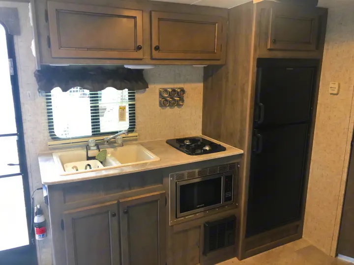 This RV rental kitchen features a double sink, stovetop, microwave, and large fridge, all built into modern gray cabinetry.. Coachmen Apex Nano 2019