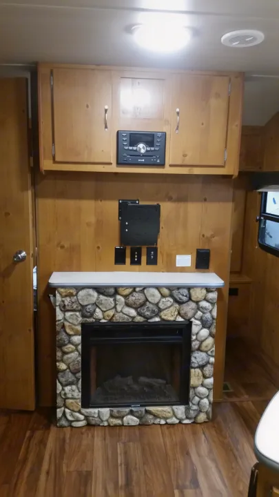Cozy RV rental interior featuring a stone-look electric fireplace, wood cabinets, and an entertainment system.. Gulfstream Cabin Cruiser 2018