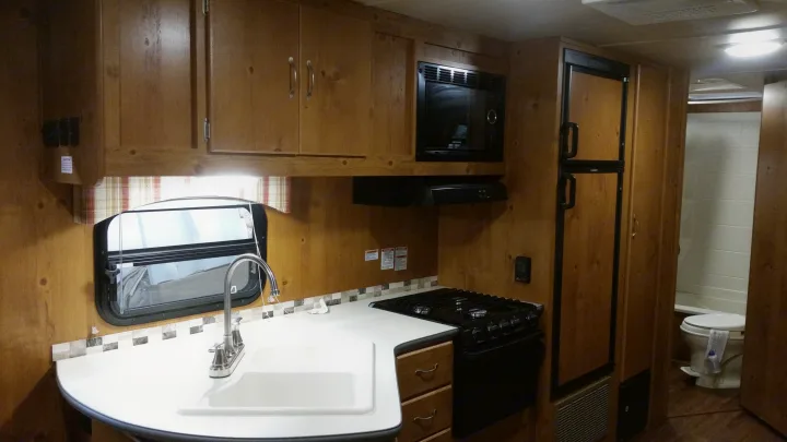 Spacious RV rental kitchen featuring wood cabinets, microwave, stove, sink, fridge, and a glimpse of the bathroom.. Gulfstream Cabin Cruiser 2018