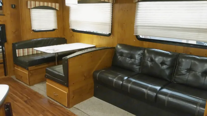Inside an RV rental: a black leather dinette with a table and a comfy sofa, framed by wood paneling and blinds.. Gulfstream Cabin Cruiser 2018