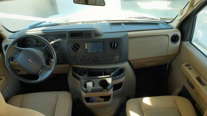 Interior of an **rv rental** cockpit, showing the Ford steering wheel, dashboard with multimedia system, and light-colored front seats.. Thor Motor Coach Four Winds 2019