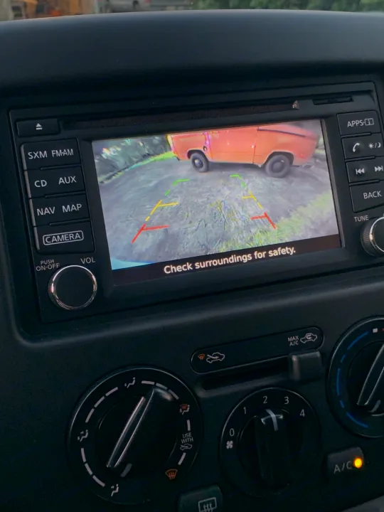 Dashboard screen shows an orange RV rental in rearview camera view, with parking lines and a safety message.. Nissan NV200 2019