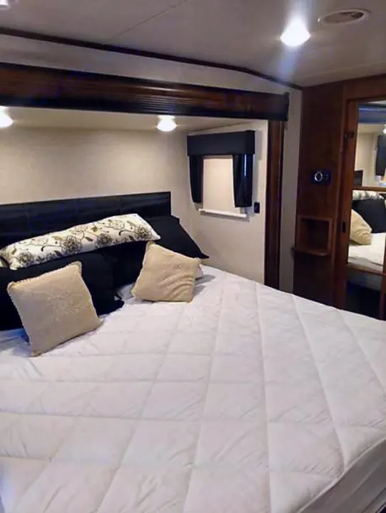 Spacious RV rental bedroom with comfortable bed, overhead lighting, and window, perfect for travel.. Heartland Big Country 2016