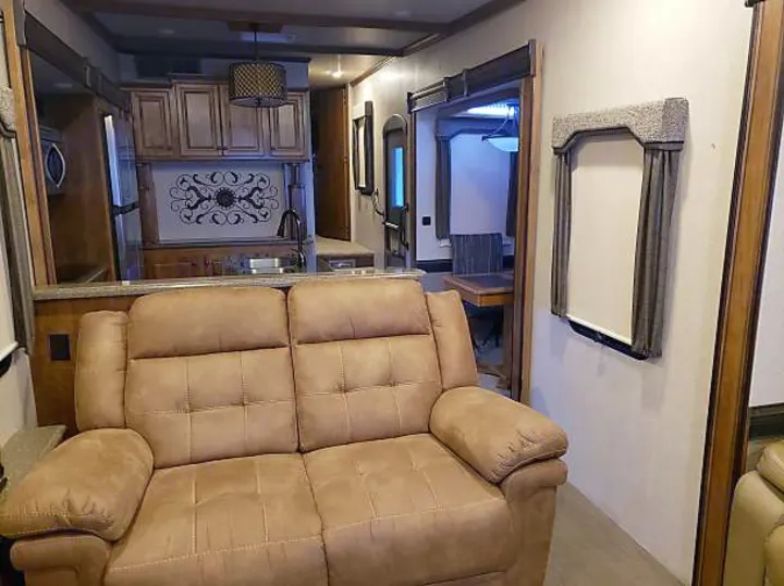 Comfortable RV rental interior showcasing a tan reclining sofa, kitchen with ornate backsplash, and dining area.. Heartland Big Country 2016