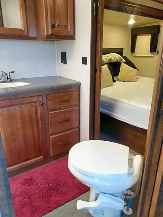 Compact RV rental interior featuring a bathroom with vanity and toilet, beside a cozy bedroom.. Heartland Big Country 2016