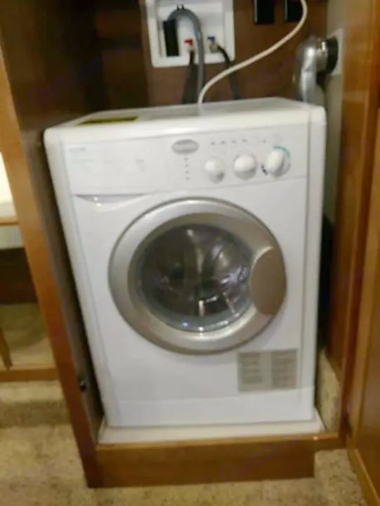 A white, compact front-load washing machine is nestled within an RV rental, demonstrating available laundry amenities for travel.. Heartland Big Country 2016