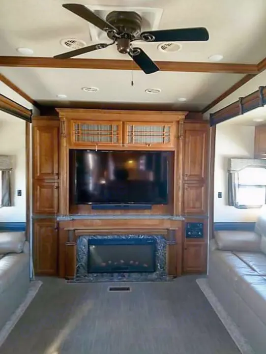 Inside a modern RV rental: cozy living room with TV, electric fireplace, ceiling fan, and seating areas.. Heartland Big Country 2016
