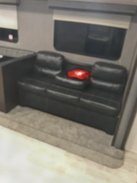 Comfortable black sofa in this RV rental, featuring window blinds and a cozy living space, perfect for travel.. Heartland Trail Runner 2020