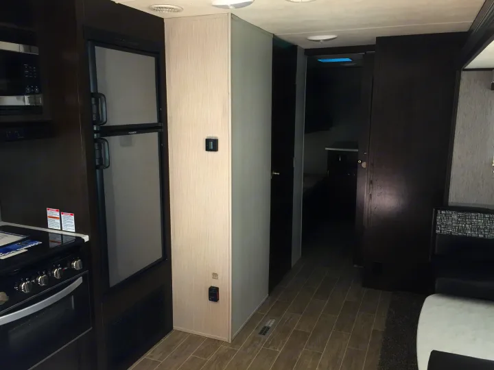Spacious RV rental interior, showing kitchen with fridge & oven, a hallway leading to bunk beds, and part of the living area.. Heartland Trail Runner 2020