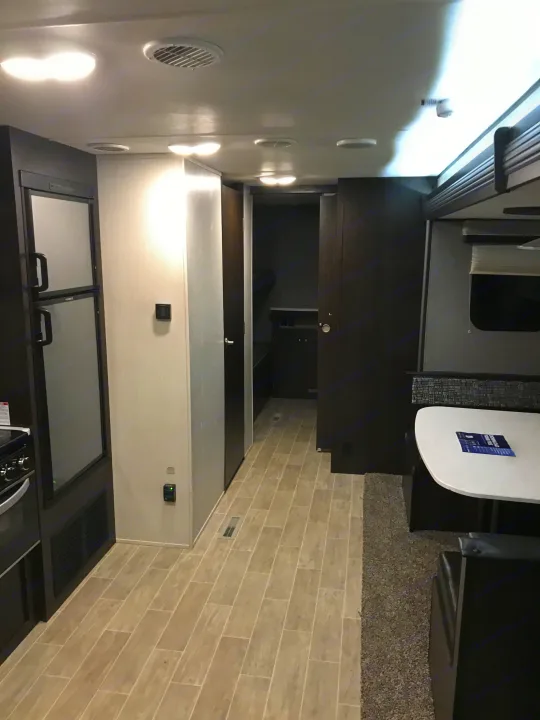 RV rental interior features a kitchen (fridge, stove), dining booth, and aisle with light flooring and modern dark cabinetry.. Heartland Trail Runner 2020
