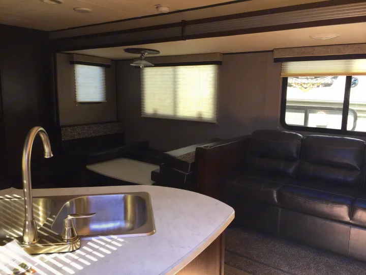 Spacious RV rental interior featuring a kitchen sink, dinette, and comfortable dark sofa, ideal for travel.. Heartland Trail Runner 2020