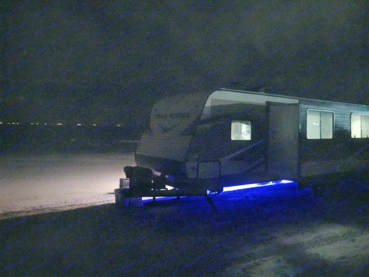 An RV rental illuminated by blue underglow lights and interior lights at night, parked in a dark, open area.. Heartland Trail Runner 2020