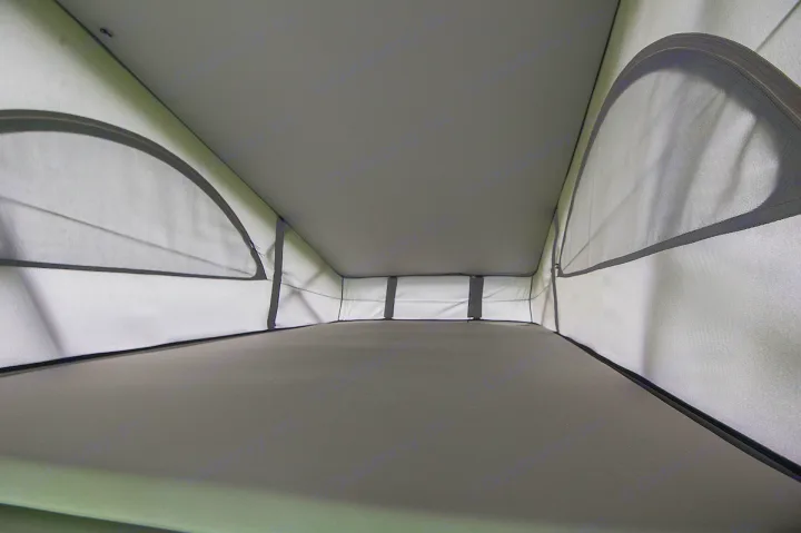 Interior of an RV rental pop-top bed area, showing the ceiling, sleeping platform, and mesh ventilation windows.. Volkswagen California Ocean 2024