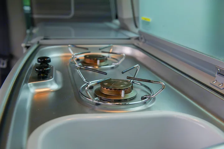 RV rental's compact stainless steel kitchen, featuring a two-burner stove and sink, ideal for travel cooking.. Volkswagen California Ocean 2024