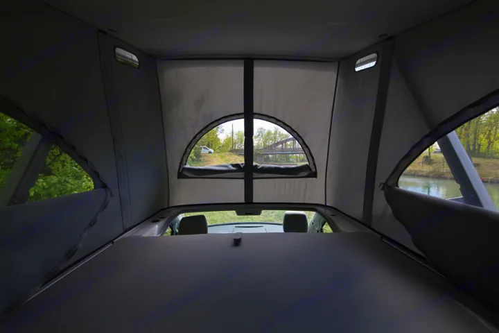 The interior of an rv rental pop-top camper shows a comfy sleeping area with clear outdoor views of a river and bridge.. Volkswagen California Coast T6 2022