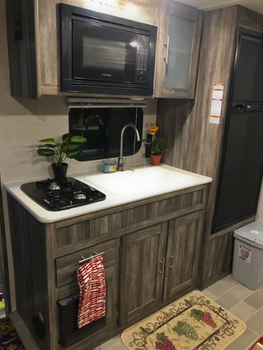 A modern RV rental kitchen featuring a microwave, two-burner stove, sink, cabinets, and a compact fridge. Ideal for travel.. Forest River Salem 2020