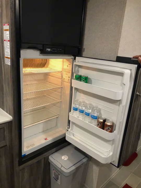 An RV rental fridge open, revealing its interior with water bottles, root beer, and Sprite on door shelves. Perfect for RV travel.. Forest River Salem 2020