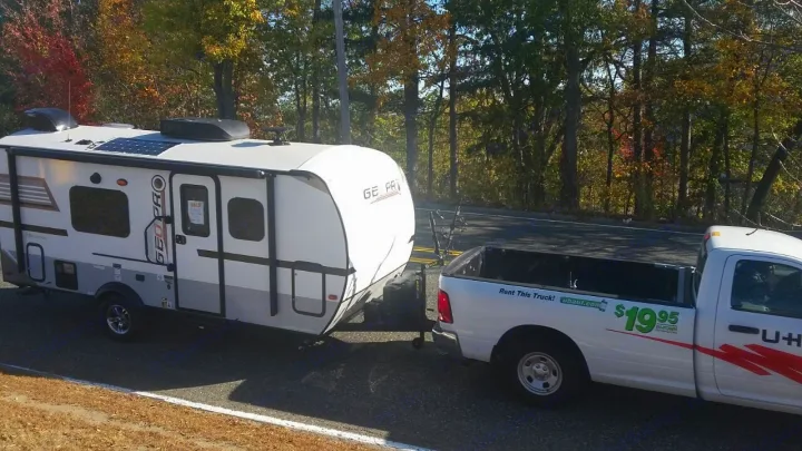 U-Haul truck towing a Geo Pro RV rental, a white travel trailer, on a road with autumn trees, ready for adventure.. Forest River Rockwood 2018