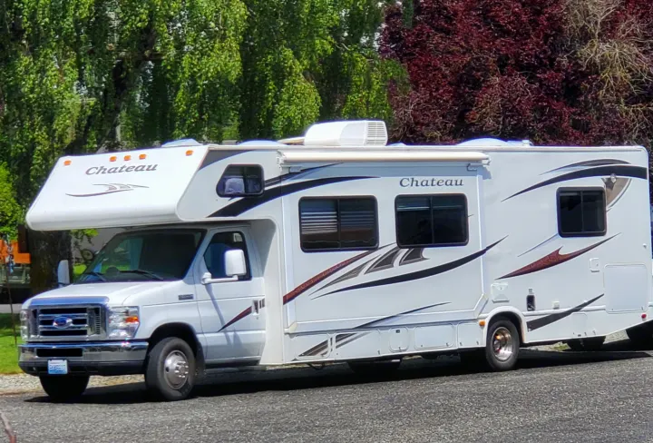 White Ford Chateau Class C RV rental, ready for adventure, parked on asphalt with lush trees in the background.. Ford Fourwinds 2012