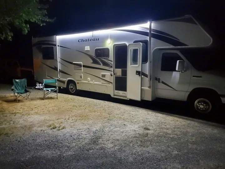 Brightly lit Chateau RV rental at night. Camping chairs are set up on the gravel next to the motorhome.. Ford Fourwinds 2012