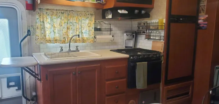 This inviting RV rental kitchen boasts a modern sink, stove, fridge, microwave, and cheerful sunflower curtains.. Ford Fourwinds 2012