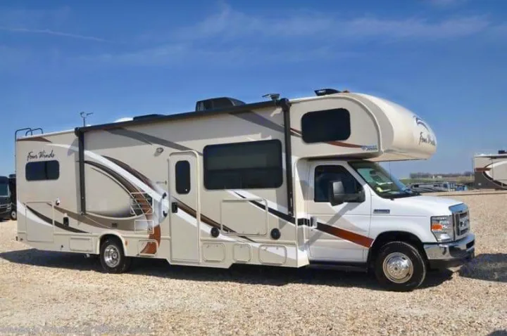 A large, modern Class C RV in light colors with dark stripes is ready for an rv rental adventure, parked on gravel.. Thor Motor Coach Four Winds 2017