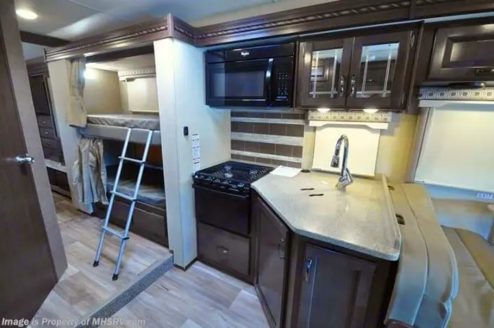 RV rental interior featuring bunk beds with a ladder, a functional kitchen with microwave, stove, and sink, plus dinette seating. Ideal for family travel.. Thor Motor Coach Four Winds 2017
