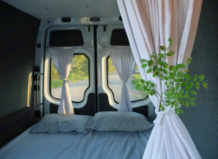 Cozy RV rental interior with a bed, light curtains, and a sprig of leaves. Enjoy nature views from this comfy campervan.. Mercedes-Benz Sprinter 2017