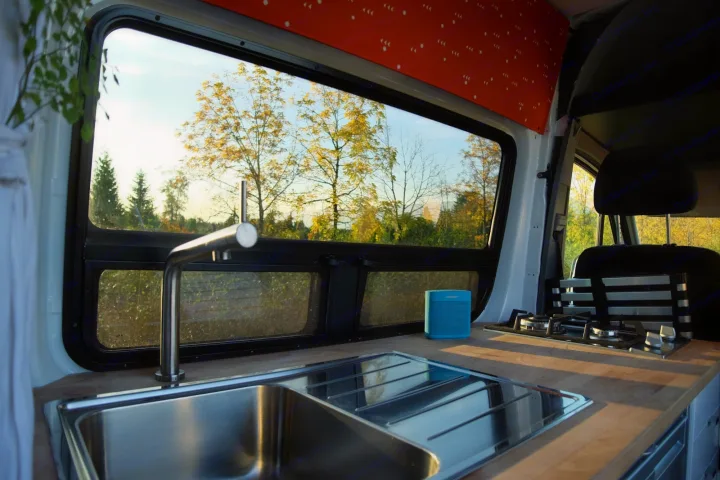 RV rental: A well-equipped camper van kitchen with a stainless steel sink, stove, and a serene view of autumn trees.. Mercedes-Benz Sprinter 2017