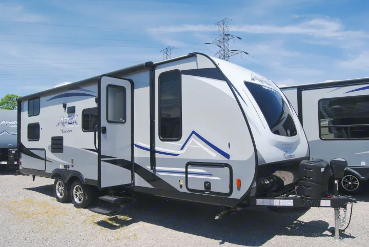A modern grey Coachmen Apex Ultra Lite travel trailer, a great rv rental option, parked on gravel under a blue sky.. Apex Nano 245 BHS 2020