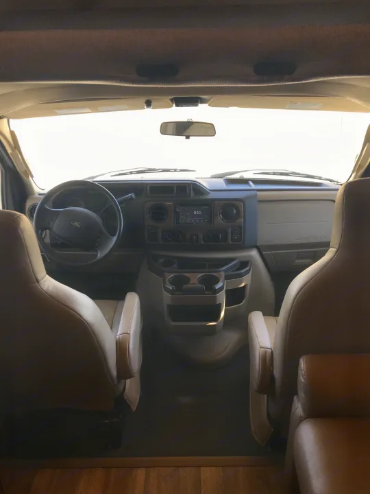 Inside an RV rental's front cabin, featuring a Ford dashboard, steering wheel, and comfortable swivel seats.. Thor Motor Coach Four Winds 2017