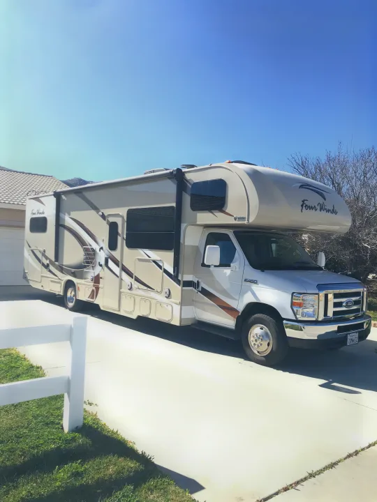 A tan and white Four Winds RV rental is parked on a sunny driveway, ready for travel. Ideal motorhome or camper.. Thor Motor Coach Four Winds 2017