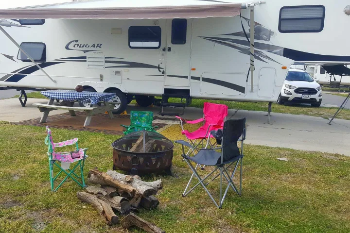 RV rental: A white travel trailer campsite with picnic table, fire pit, logs, and colorful camping chairs for relaxation.. Keystone Cougar 2008
