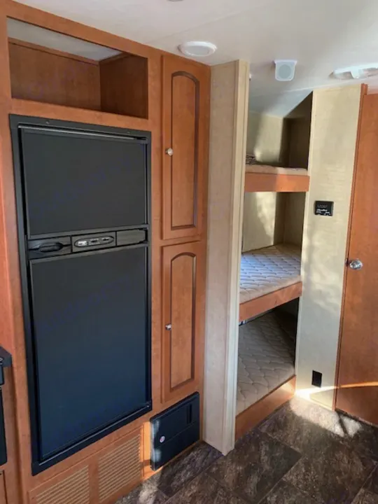 This RV rental interior shows a compact living space with bunk beds, a cooktop, and storage cabinets.. Shasta Revere 2012